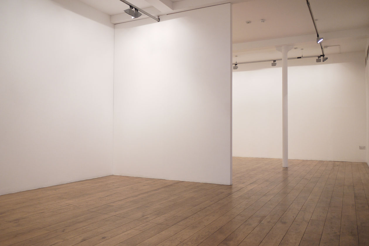 Four Corners' empty gallery with white walls, wooden flooring, and lights on the ceiling.