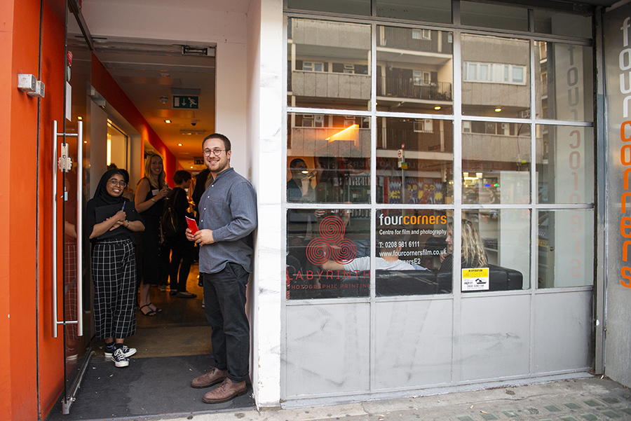 A young man and a young woman stand in the open doorway of Four Corners' building, smiling.