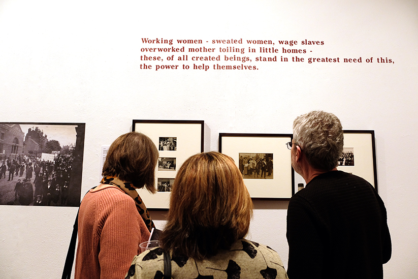 Three people standing in a gallery looking at framed black and white photographs. 