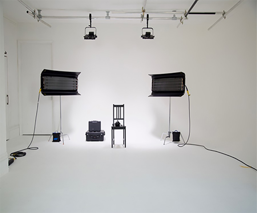 White infinity studio with two large black box lights, a black chair, and some wires and boxes.