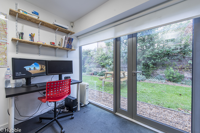 Office space with desk setup and large window and door with views onto small courtyard. O