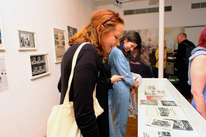 Two women in a busy gallery, looking into a glass display case filled with documents. 