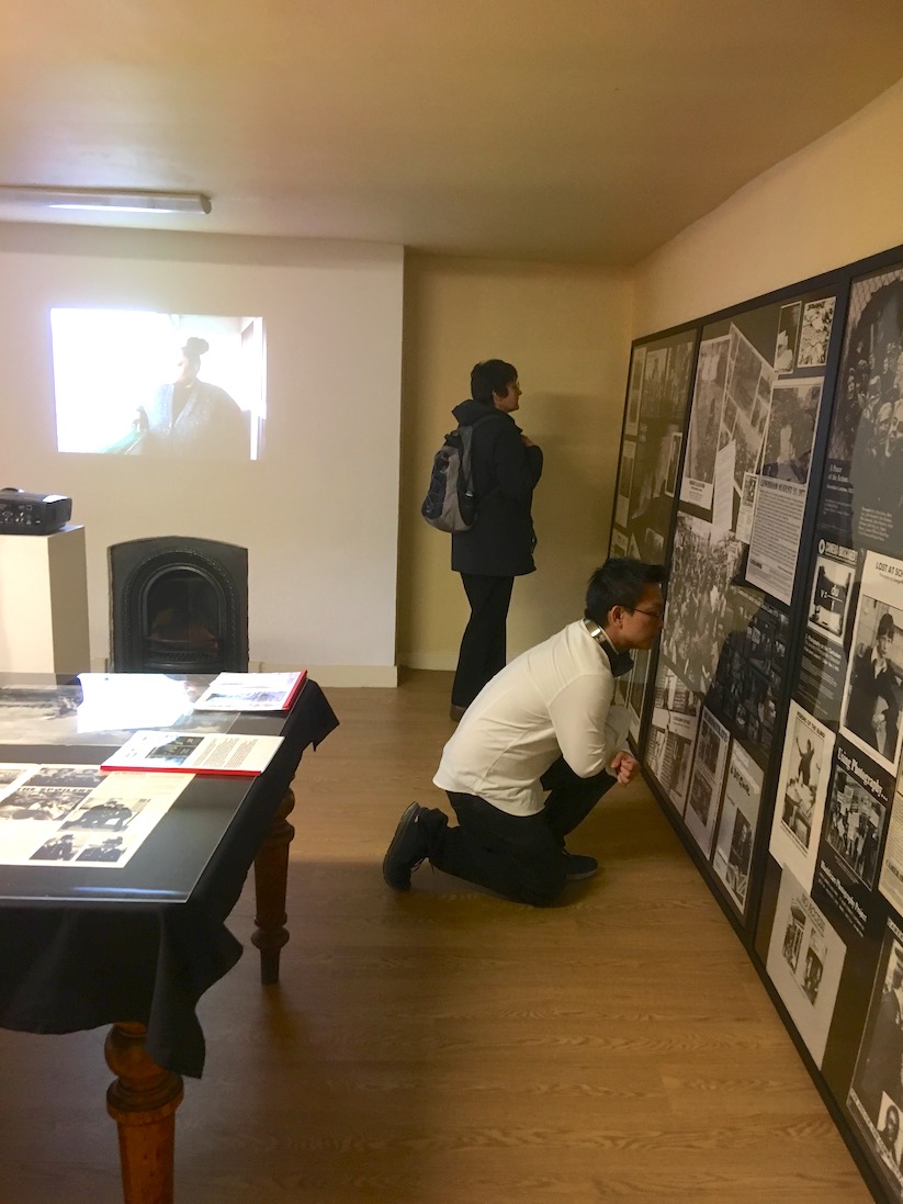 Two people look at documents and photographs arranged in two very large frames. 