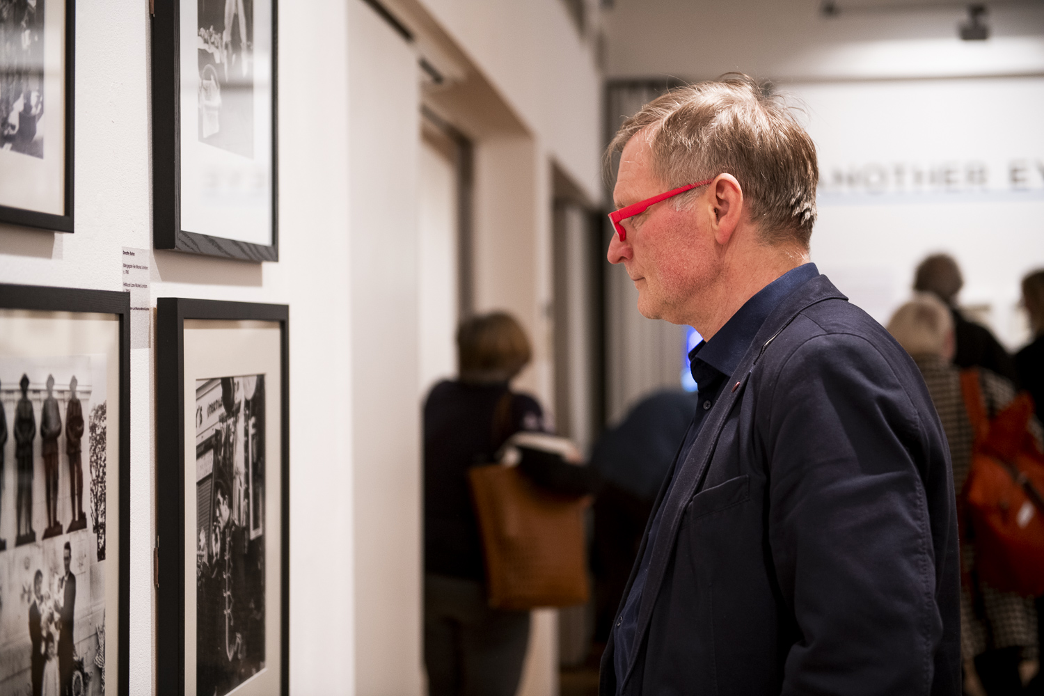 Person with red glasses looks at framed photographs on the gallery wall 