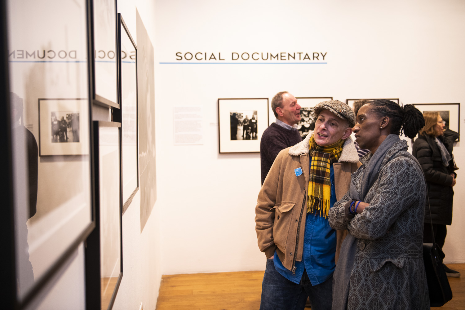 Two people talk to each other while looking at framed photographs in the gallery 