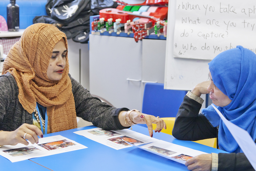 Two women sit at a table looking at photographs.