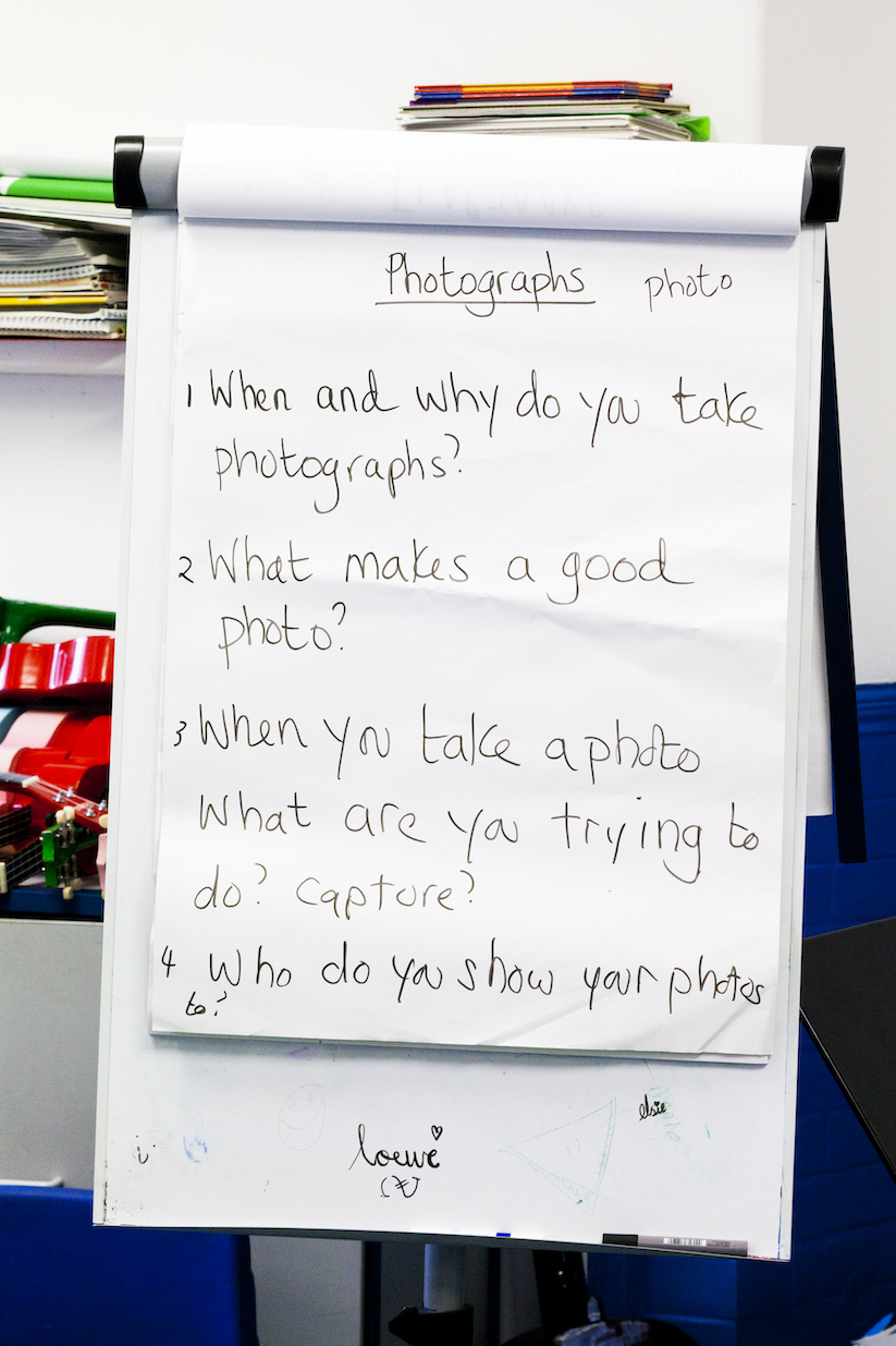 Whiteboard reads: 'Photographs. 1: When and why do you take photographs? 2: What makes a good photo? 3: When you take a photo what are you trying to do? Capture? 4: Who do you show your photos to?